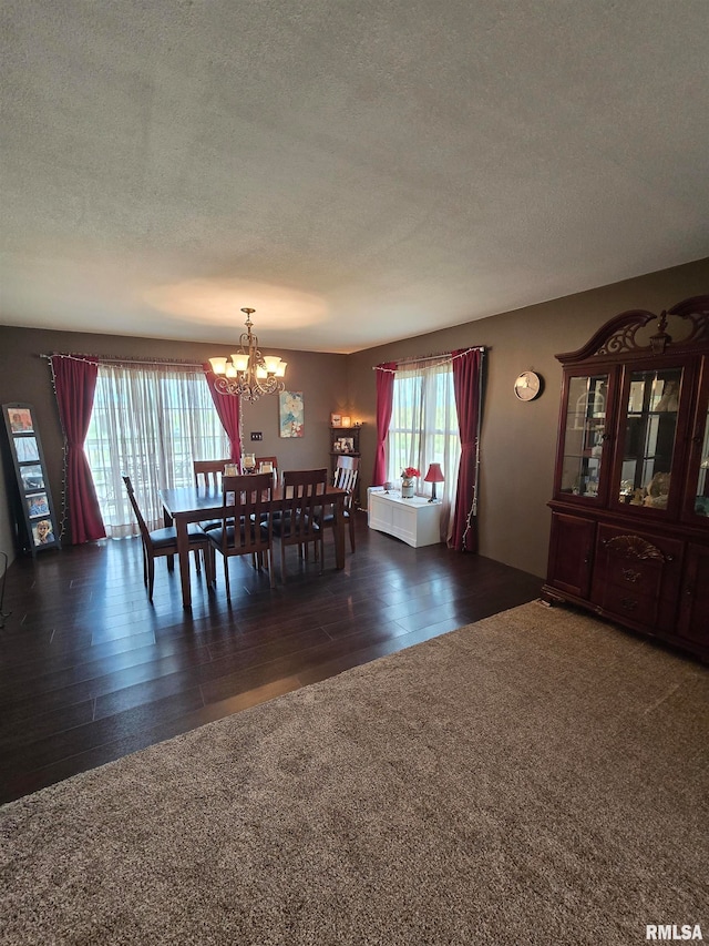 dining space featuring dark wood-type flooring, a textured ceiling, and a chandelier