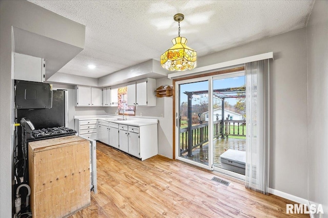 kitchen with white cabinetry, light wood-type flooring, a textured ceiling, hanging light fixtures, and sink