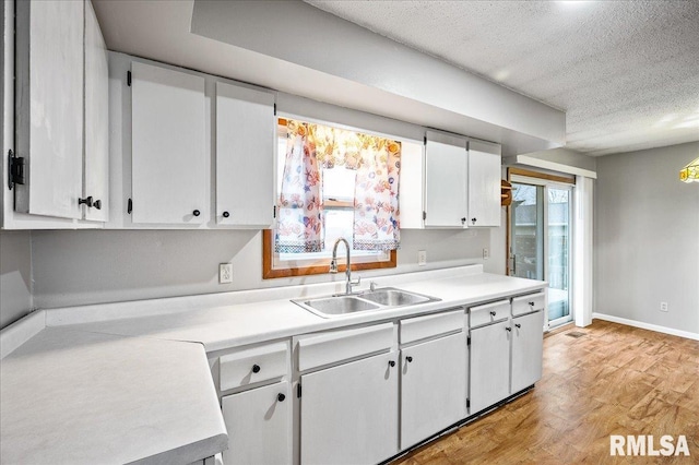 kitchen with light hardwood / wood-style flooring, a textured ceiling, sink, and white cabinets