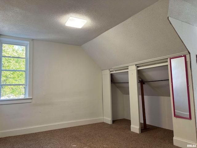 unfurnished bedroom with lofted ceiling, dark colored carpet, and a textured ceiling