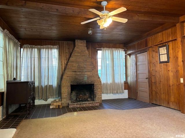 unfurnished living room featuring a fireplace, wooden ceiling, dark carpet, wood walls, and ceiling fan