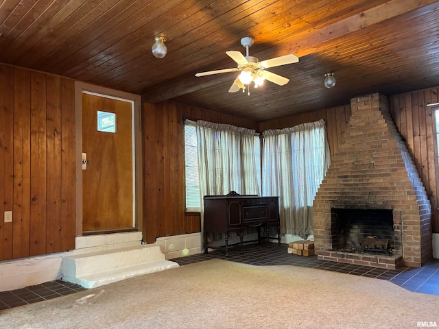 living room featuring wood walls, a brick fireplace, ceiling fan, wood ceiling, and dark colored carpet