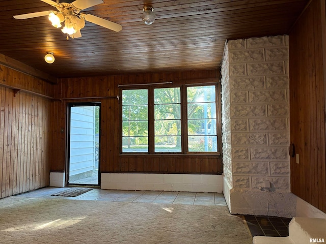 unfurnished living room featuring wood ceiling, ceiling fan, wood walls, and light tile patterned flooring