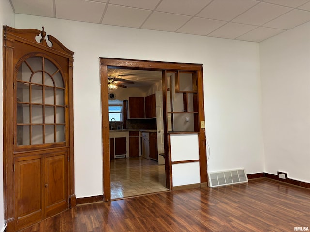 empty room featuring dark wood-type flooring, sink, ceiling fan, and a drop ceiling