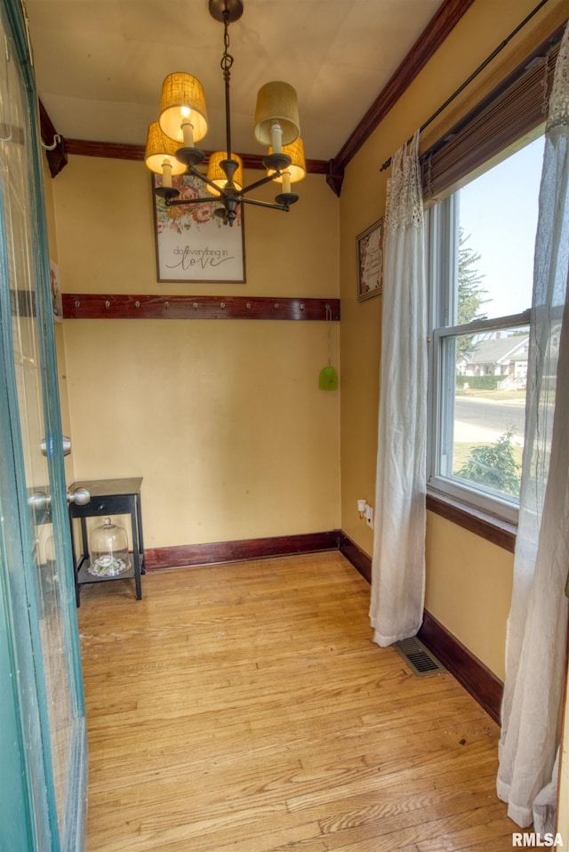 unfurnished dining area featuring a chandelier, light wood-type flooring, and ornamental molding