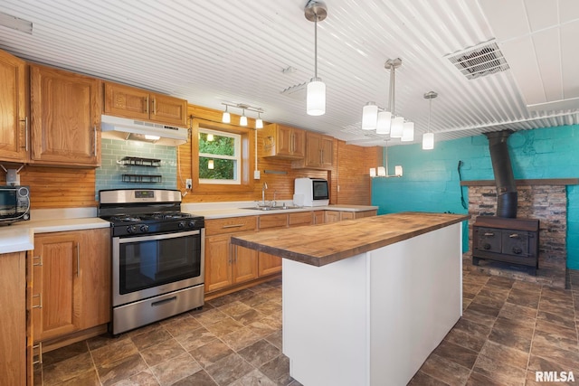 kitchen with sink, butcher block counters, a wood stove, hanging light fixtures, and gas range