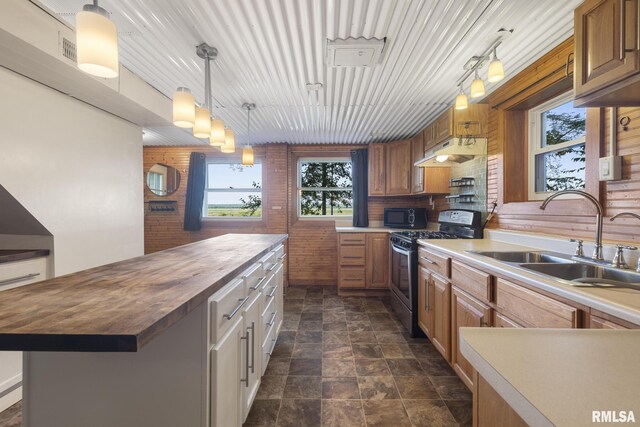 kitchen featuring butcher block counters, hanging light fixtures, brick wall, sink, and stainless steel gas range oven