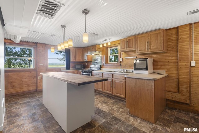 kitchen with stainless steel range with gas stovetop, sink, a wealth of natural light, and decorative light fixtures