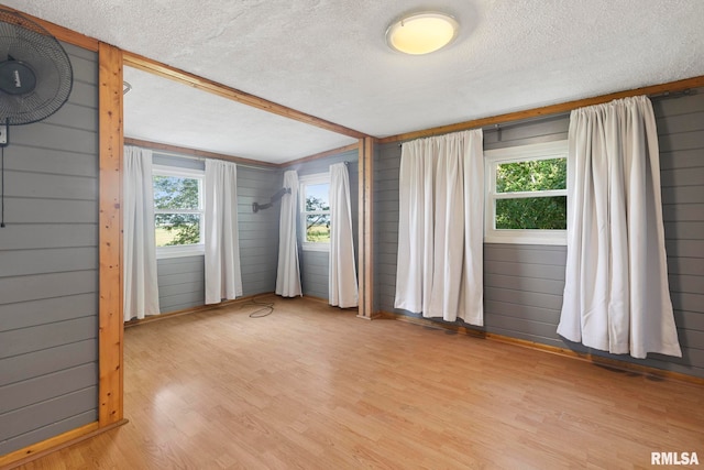 spare room featuring a textured ceiling, light hardwood / wood-style flooring, and wooden walls