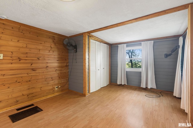 unfurnished bedroom featuring light hardwood / wood-style floors, a textured ceiling, and wooden walls