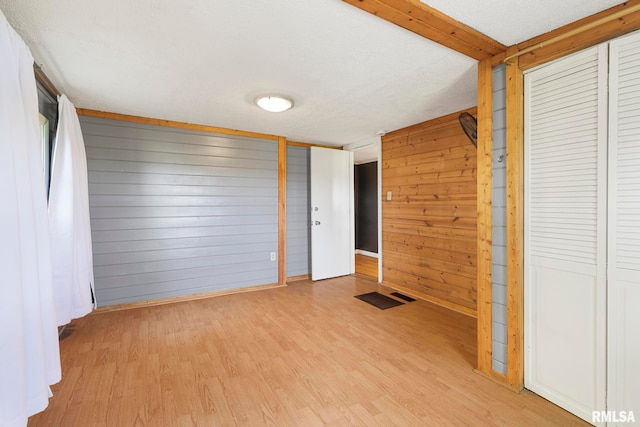 interior space with light hardwood / wood-style flooring, a textured ceiling, a closet, and wood walls