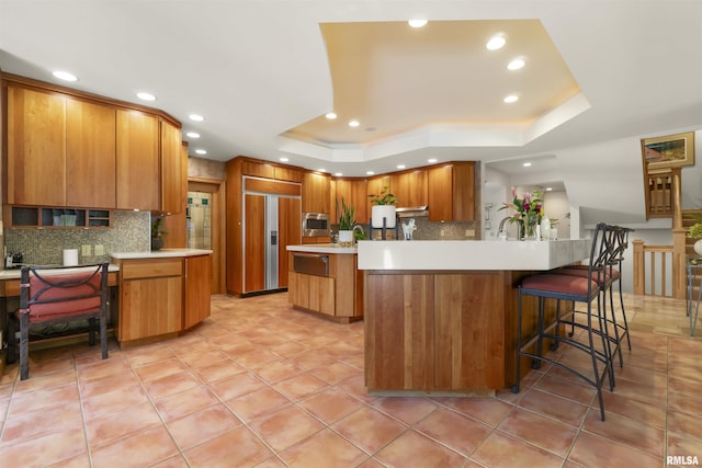 200 W Ravinwoods Rd, Peoria, IL 61615 - kitchen featuring built in appliances, a raised ceiling, tasteful backsplash, light countertops, and recessed lighting