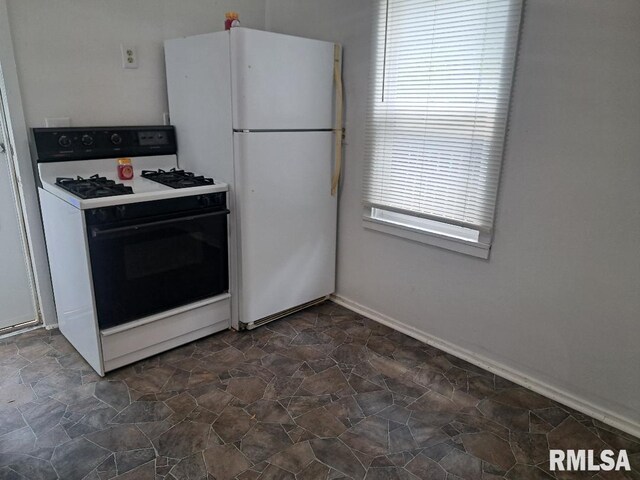 kitchen featuring range with gas cooktop, freestanding refrigerator, and stone finish flooring