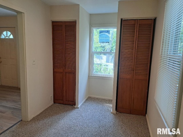 unfurnished bedroom with light carpet, two closets, and baseboards