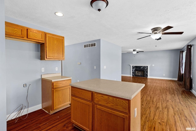 kitchen featuring ceiling fan, a high end fireplace, dark hardwood / wood-style flooring, and a kitchen island