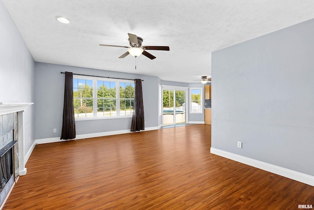 unfurnished living room with hardwood / wood-style flooring, ceiling fan, a textured ceiling, and a tiled fireplace