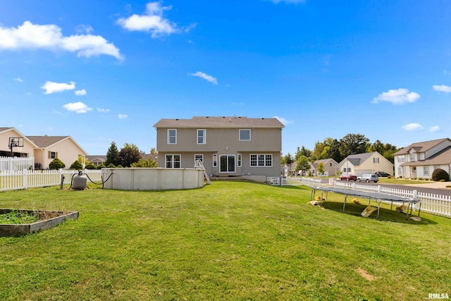 rear view of house featuring a trampoline and a yard