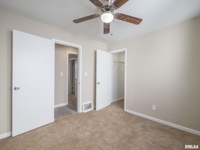 unfurnished bedroom with a spacious closet, ceiling fan, light colored carpet, and a closet