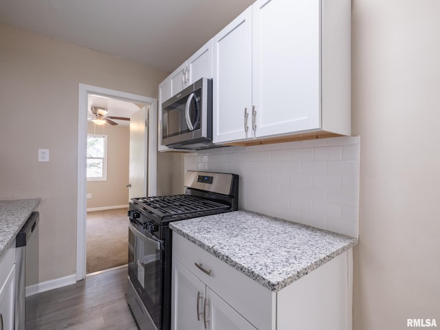 kitchen with light stone counters, white cabinetry, decorative backsplash, stainless steel appliances, and ceiling fan