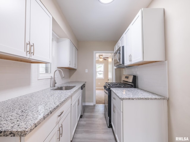 kitchen featuring stainless steel appliances, white cabinets, light stone counters, and sink