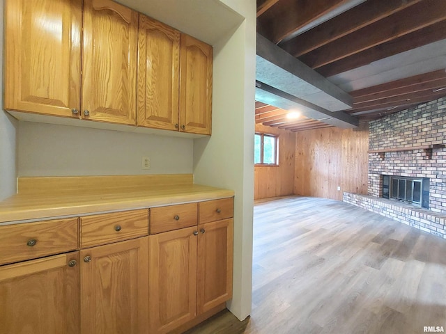 kitchen featuring wood walls, light hardwood / wood-style floors, beamed ceiling, and a fireplace