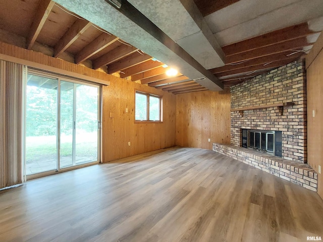 unfurnished living room featuring light wood-type flooring, beam ceiling, wood walls, and a brick fireplace