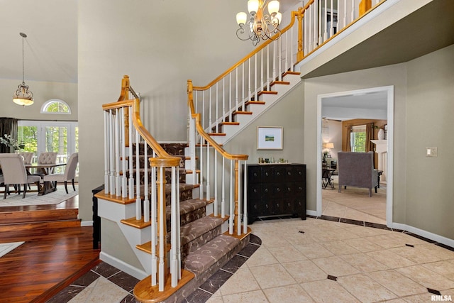 staircase with a towering ceiling, a chandelier, and a healthy amount of sunlight