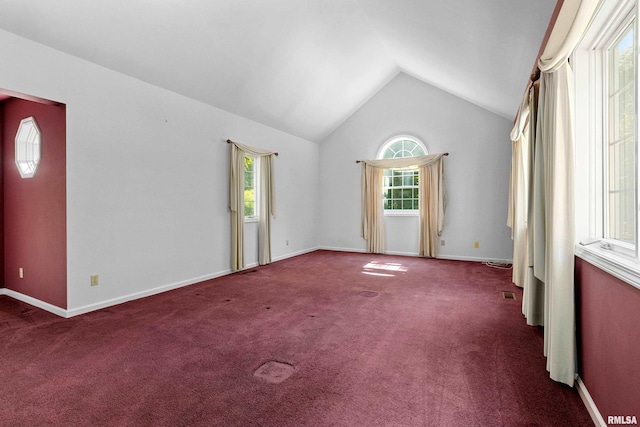 unfurnished room featuring lofted ceiling, dark colored carpet, and a healthy amount of sunlight