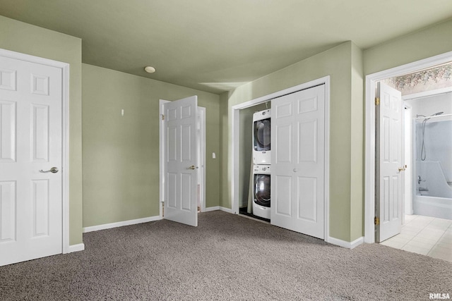 unfurnished bedroom featuring stacked washer and dryer, light colored carpet, and ensuite bathroom