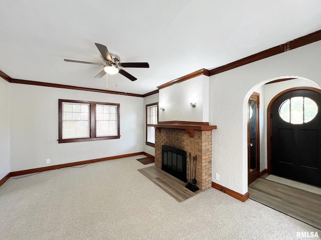 unfurnished living room featuring ceiling fan, a fireplace, light carpet, and crown molding