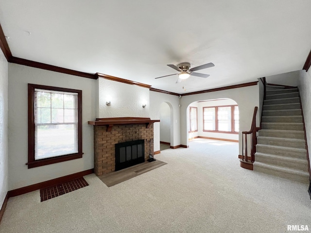 unfurnished living room with carpet floors, crown molding, ceiling fan, and a brick fireplace