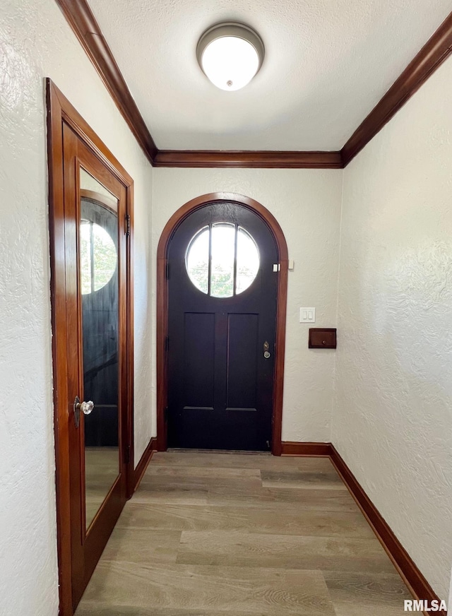 doorway to outside with ornamental molding, a textured ceiling, and light hardwood / wood-style floors