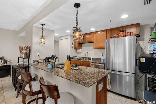 kitchen featuring hanging light fixtures, dark stone countertops, light tile patterned floors, kitchen peninsula, and stainless steel appliances