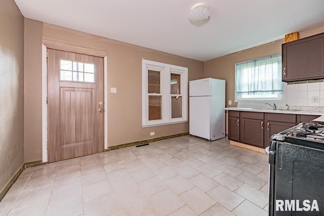 kitchen featuring decorative backsplash, dark brown cabinets, black range, and white refrigerator