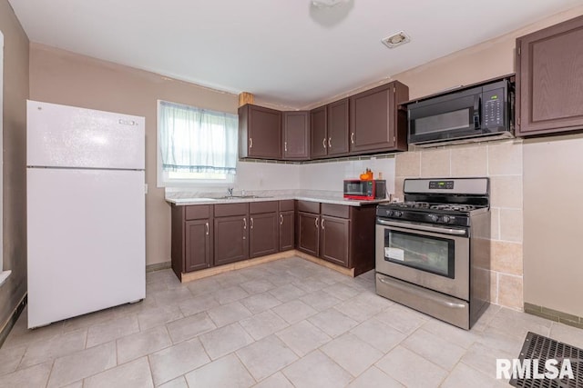 kitchen with sink, stainless steel gas range, tasteful backsplash, white fridge, and dark brown cabinetry