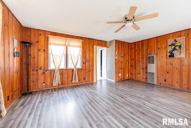 unfurnished living room featuring ceiling fan, wood walls, and light wood-type flooring