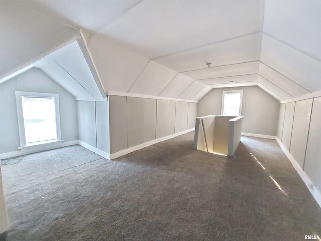 additional living space featuring dark colored carpet, plenty of natural light, and vaulted ceiling