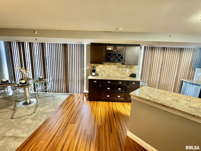 kitchen with light stone counters, light hardwood / wood-style floors, dark brown cabinetry, and tasteful backsplash