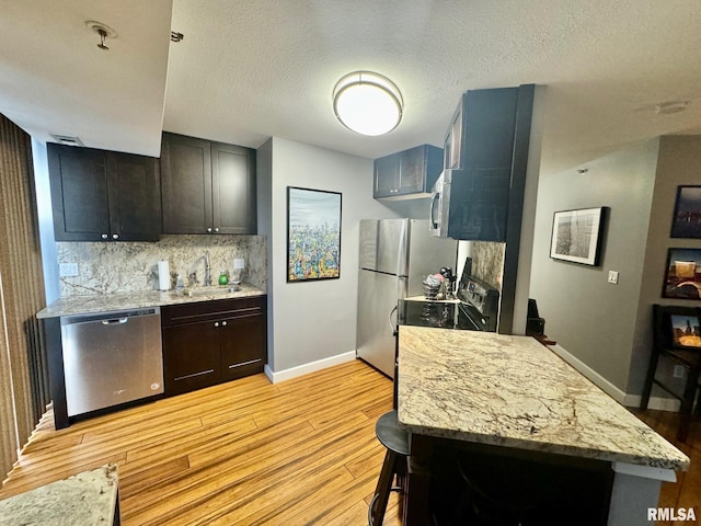 kitchen with sink, a textured ceiling, stainless steel appliances, light stone countertops, and light hardwood / wood-style floors