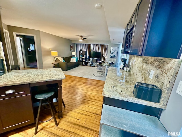 kitchen with ceiling fan, light stone counters, tasteful backsplash, a breakfast bar area, and light wood-type flooring