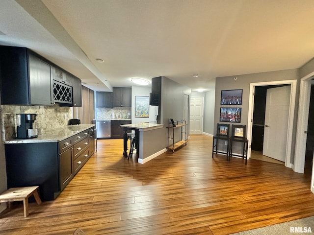 kitchen featuring light wood-type flooring, stainless steel dishwasher, a kitchen island, and a breakfast bar