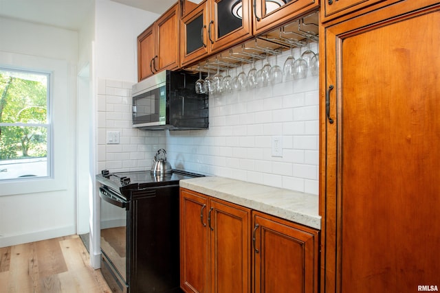 kitchen with backsplash, black stove, light hardwood / wood-style flooring, and light stone counters