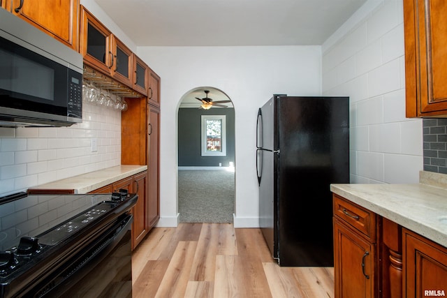 kitchen featuring backsplash, light stone countertops, light wood-type flooring, black appliances, and ceiling fan