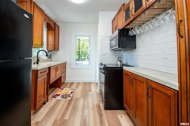 kitchen featuring light wood-type flooring, sink, tasteful backsplash, black appliances, and light stone countertops