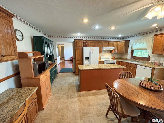 kitchen featuring light stone counters, white appliances, a kitchen island, ceiling fan, and sink