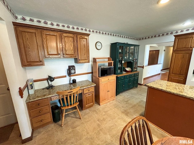 kitchen with a textured ceiling, light stone countertops, and built in desk