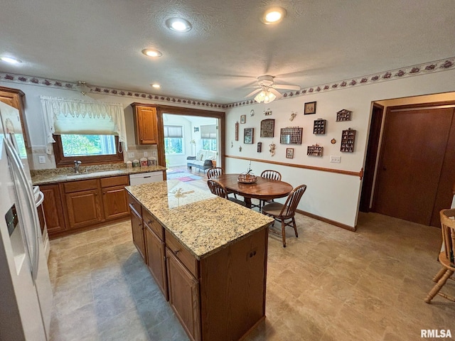 kitchen with a textured ceiling, a kitchen island, white appliances, light stone countertops, and ceiling fan