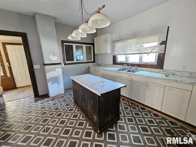 kitchen with light stone counters, hanging light fixtures, sink, and a kitchen island