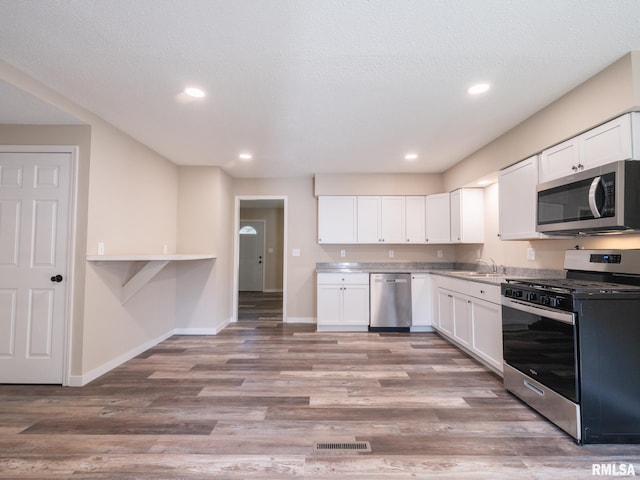 kitchen with appliances with stainless steel finishes, light hardwood / wood-style floors, sink, and white cabinets