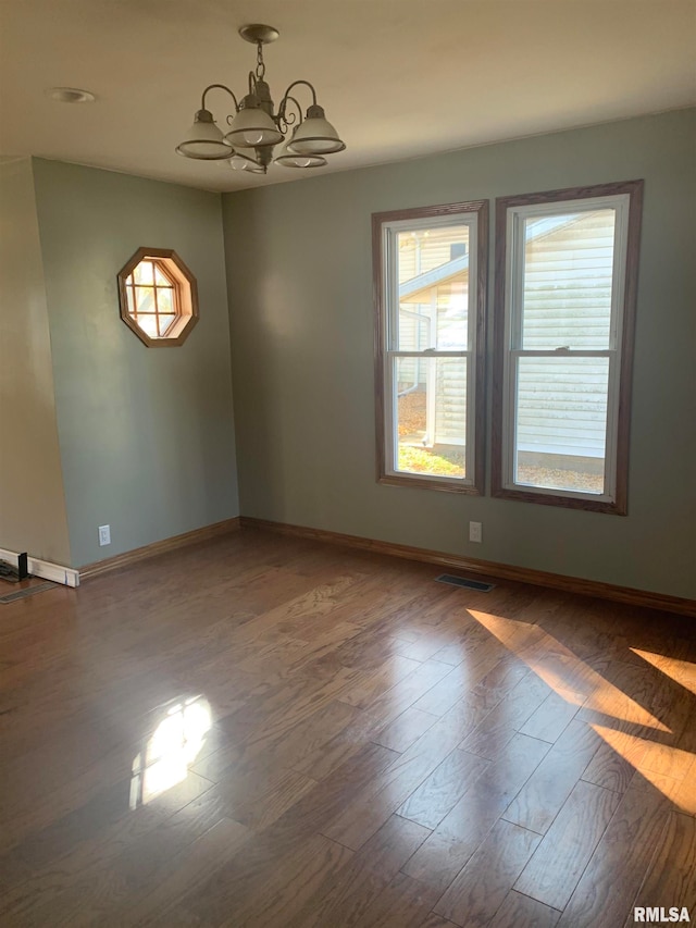 spare room with wood-type flooring and an inviting chandelier